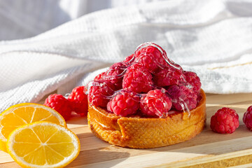 Pink fresh raspberry tart and fresh lemons on the kitchen table background.