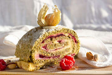 Green pistachio meringue roulade slice with raspberry jelly jam on light wooden board background in...