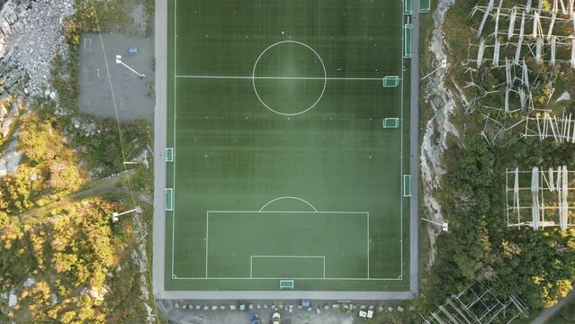 Upwards flying aerial drone footage revealing the spectacular football soccer stadium of Henningsvaer at Lofoten, Norway situated on a lonely island with the ocean and mountains surrounding it