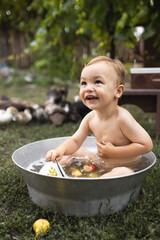 Little funny boy is bathing in a big metal trough. A child bathes in a trough surrounded by ducks. Village fun. Rural life. Happy childhood. The child is bathing in the garden.