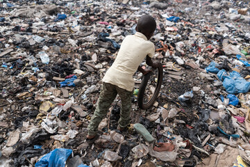 Top view of a small African boy playing with an old bike tire in a heavily polluted area; symbol of...