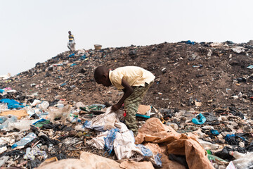 Small African boy busy recycling objects amidst heaps of plastic waste and dirt in an urban...