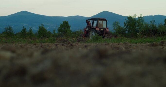 Tractor driver finished work after a hard day's work. Tractor harvests against the backdrop of high mountains at sunset