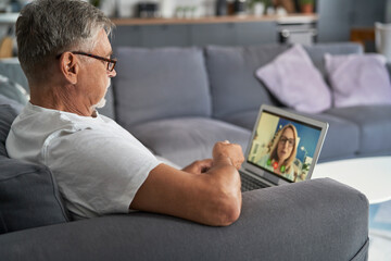 Fototapeta na wymiar Senior caucasian man sitting at the couch and talking by video call