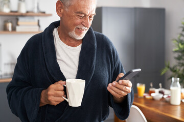 Senior caucasian man using mobile phone and drinking coffee at morning