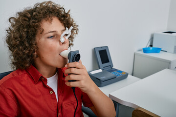 Curly boy performing pulmonary function test and spirometry using spirometer at medical clinic. Spirometry of child's lungs - obrazy, fototapety, plakaty