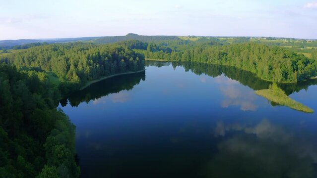 Aerial view of a calm lake reflecting the sky surrounded by forest in Poland.