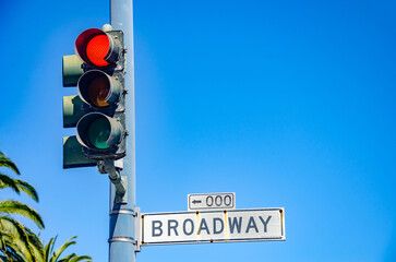 A red traffic light and a street sign for 'Broadway' against a clear blue summer sky in San Francisco, California
