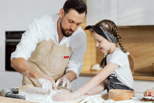 Delighted young frather wearing apron teach daughter kneading dough for baking homemade pizza.