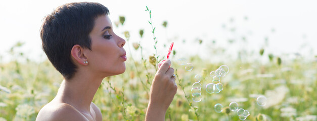 Young woman blowing soap bubbles on the sunny summer meadow