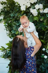 A mother with her newborn baby boy is standing in a room decorated with plants and flowers. The concept of motherhood and childhood.