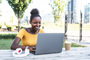 young black woman working on her laptop in a city park, student preparing exam, concept of work,...