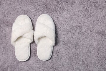 Fototapeta na wymiar Soft white slippers on fluffy grey carpet, top view. Space for text