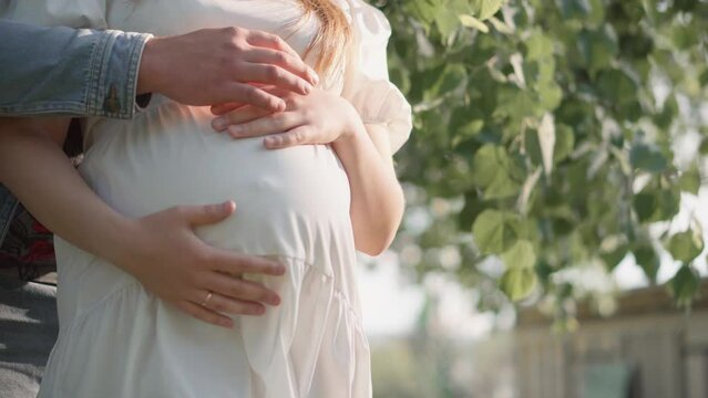 Pregnant girl and her boyfriend are hugging her tummy. Pregnancy and happiness young family. Future mother and father are waiting birth baby, their firstborn. Wife and husband are resting in the park.