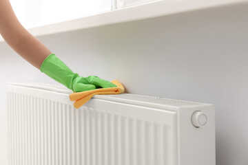 Woman cleaning radiator with rag indoors, closeup. Space for text