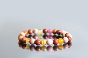 Bracelet made of natural pink agate stones beads isolated on white background. Handmade jewelry. Woman exoteric accessories. Talismans and amulets. Selective focus - obrazy, fototapety, plakaty