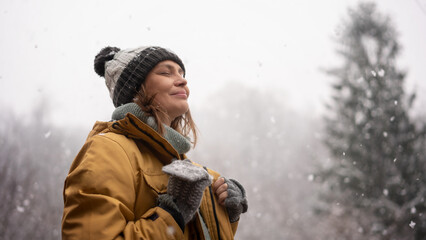 Young mature adult caucasian woman in a hat and yellow jacket breathing fresh air in the winter...