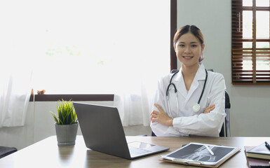 Portrait of young asian female doctor smiling and looking at camera sitting in examination room.