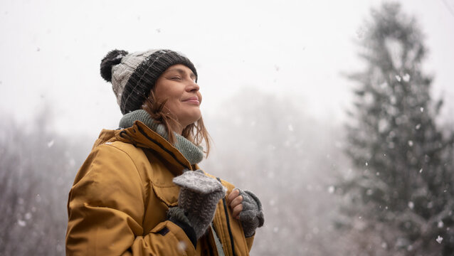Young mature adult caucasian woman in a hat and yellow jacket breathing fresh air in the winter forest