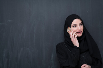 Young modern muslim business woman using smartphone wearing hijab clothes in front of black chalkboard