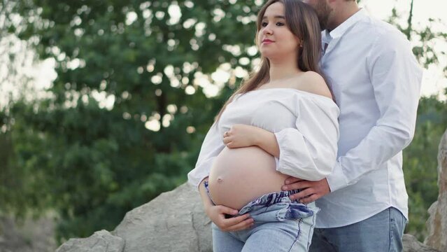 Pregnant girl and her boyfriend are hugging her tummy. Pregnancy and happiness young family. Future mother and father are waiting birth baby, their firstborn. Wife and husband are resting in the park.