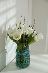 Beautiful bouquet of willow branches and tulips in vase near white wall