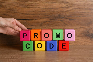 Woman making words Promo Code with colorful cubes at wooden table, closeup