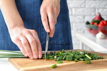 Woman cutting green spring onion on wooden board, closeup