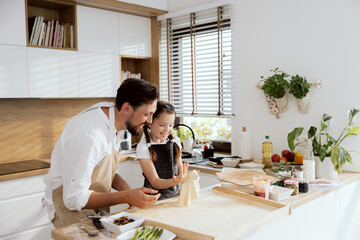 Curious daughter kid trying throw up dough rolling with hands. Father watching process managing. Happy parent spends time at weekend aith daughter preparing homemade pizza.