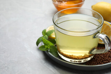 Cup of aromatic buckwheat tea, mint, honey and granules on light grey marble table, closeup. Space for text
