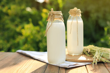 Bottles of tasty fresh milk on wooden table outdoors, space for text