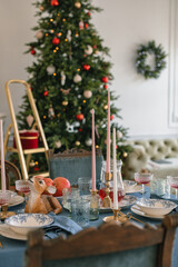 Beautifully decorated holiday table for dinner and Christmas tree in a cozy room.