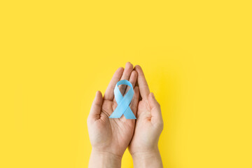 World Diabetes day. Adult hands holding blue purple ribbon on yellow background. Banner is symbol of diabetes awareness. 14 november