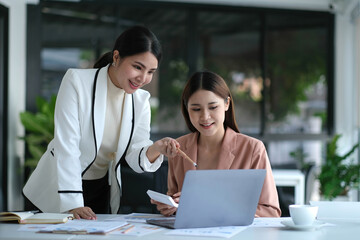 Two young Asian business woman talk, consult, discuss working with new startup project idea presentation analyze plan marketing and investment in the office.