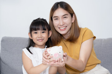 Portrait of Asian Mother and Daughter holding and show the piggy bank saving money and inverst for her daughter in future with smile.
