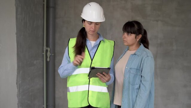 woman civil engineer or architect writes down the customer wishes for the renovation of the apartment using tablet. Sales female agent talking with client in new building.