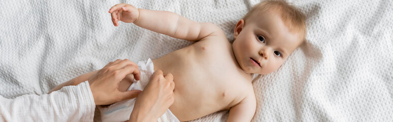 Top view of mom wearing diaper on baby daughter on bed, banner.