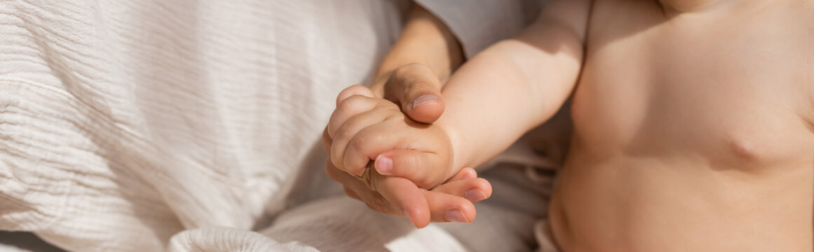 cropped view of mother holding hands with infant girl in bedroom, banner.