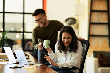 Colleagues laughing in office. Businesswoman and businessman drinking coffee