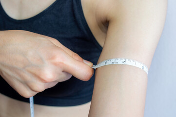 Close up of young woman in sport bra using a measuring tape for measuring her arm length.