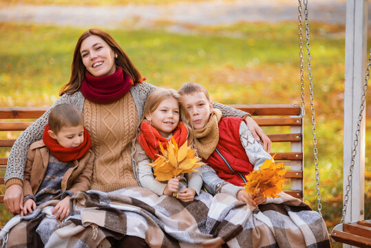 Mom And Her Children Ride On A Swing In The Park In Autumn. Woman With Three Children Walking In Nature