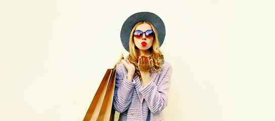 Autumn portrait of beautiful young woman with shopping bags blowing her lips sends air kiss with lipstick wearing coat, round hat on white background, blank copy space for advertising text