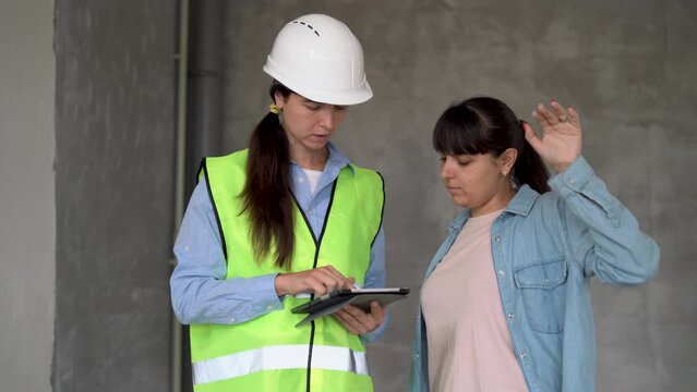 Sales Female Agent Talking With Client In New Building. Woman Working As Realtor In Construction Site With Customer. Real Estate Broker Showing Home To Woman.