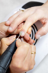 Obraz na płótnie Canvas Manicure master applying electric nail file machine removing old nail polish on fingernails