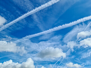 Aircraft condensation contrails in the blue sky inbetween some clouds