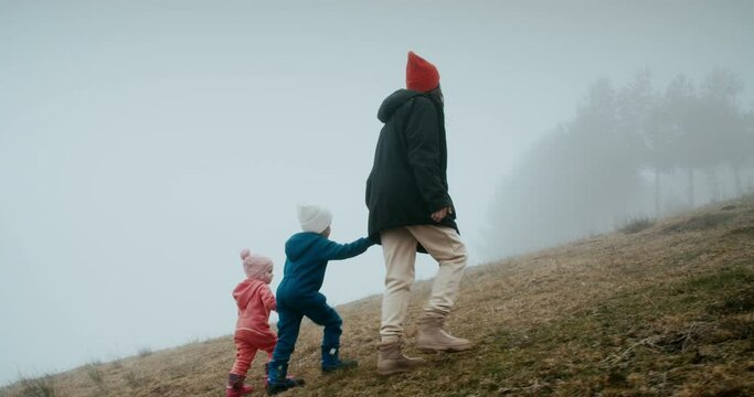 Family walk on foggy day holding hands and climbing mountain. Woman hold children hand on hiking journey at autumn weekend. 