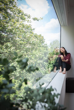 Thoughtful young woman looking at trees from window at home