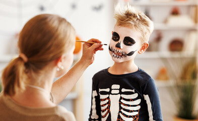 Festive makeup for Halloween. Woman doing skeleton make-up for boy in costume while preparing...