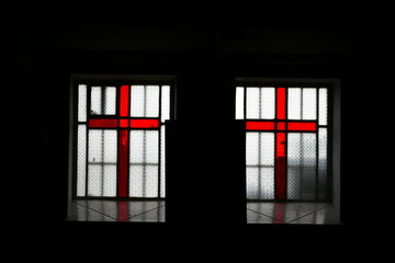 A view of two windows with red crosses inside of them back lit by the sun spotted inside of a dark cellar under one of Polish churches on a sunny day on a Polish countryside