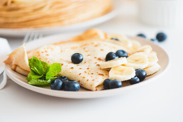 Close-up French crepes with banana and blueberries on white table